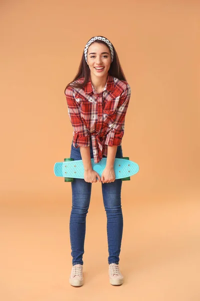 Stylish young woman with skateboard on color background