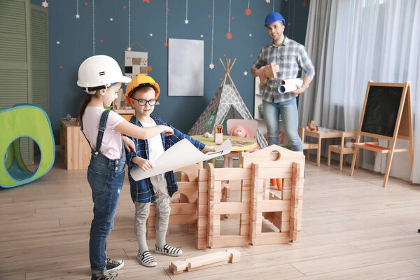 Father and little children dressed as builders playing with take-apart house at home