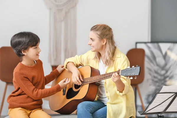 Private music teacher giving guitar lessons to little boy at home