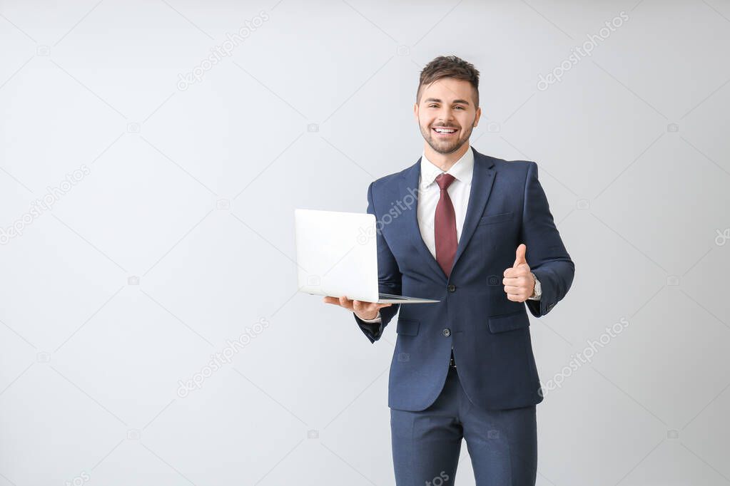 Handsome businessman with laptop showing thumb-up on light background