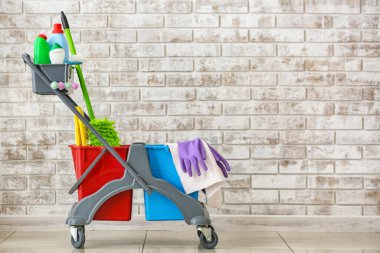 Tuğla duvarın yanında temizlik malzemeleri var.