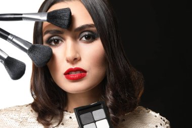 Siyah beyaz arka planda makyaj fırçası ve kozmetik ürünleri olan güzel genç bir kadın.