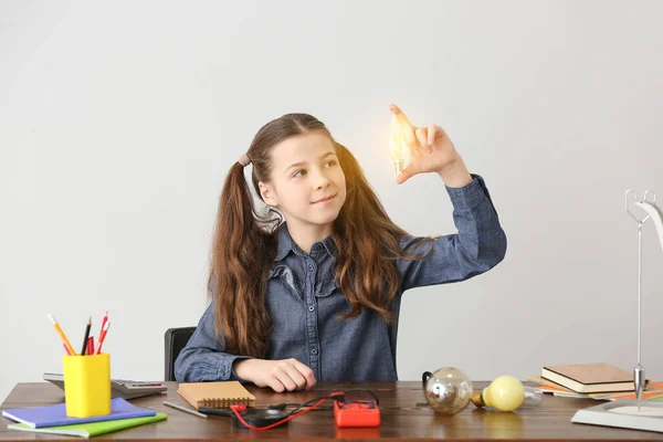 Schattig Klein Schoolmeisje Met Gloeiende Gloeilamp Aan Tafel Tegen Grijze — Stockfoto