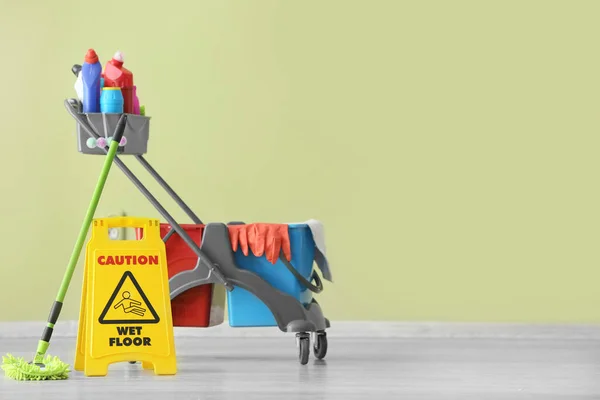 Set of cleaning supplies with caution sign near color wall