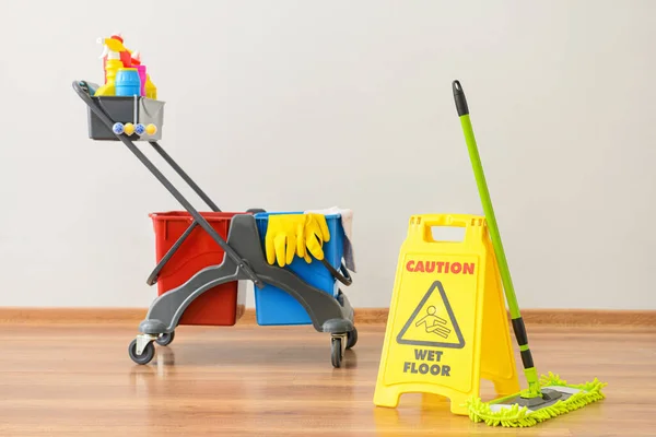 Set of cleaning supplies with caution sign near white wall