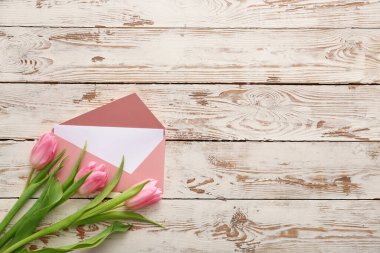 Beyaz ahşap zemin üzerinde kart ve çiçekler olan zarf