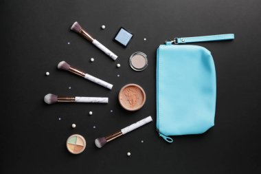 Koyu arkaplanda makyaj fırçaları ve dekoratif kozmetik ürünleri olan çanta.