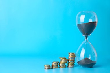 Renkli arka planda kum saati ve madeni paralar. Zaman yönetimi kavramı