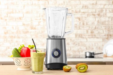 Karıştırıcı, bir bardak sağlıklı meyve püresi ve malzemeler masada.