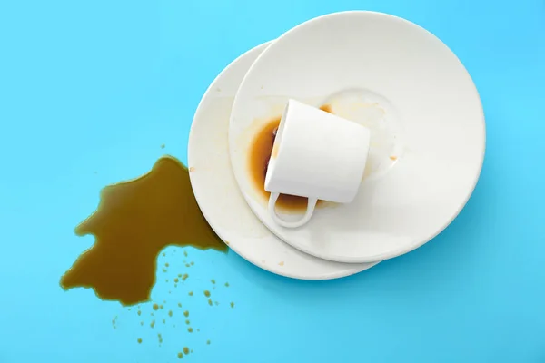 Overturned cup of coffee and plates on color background