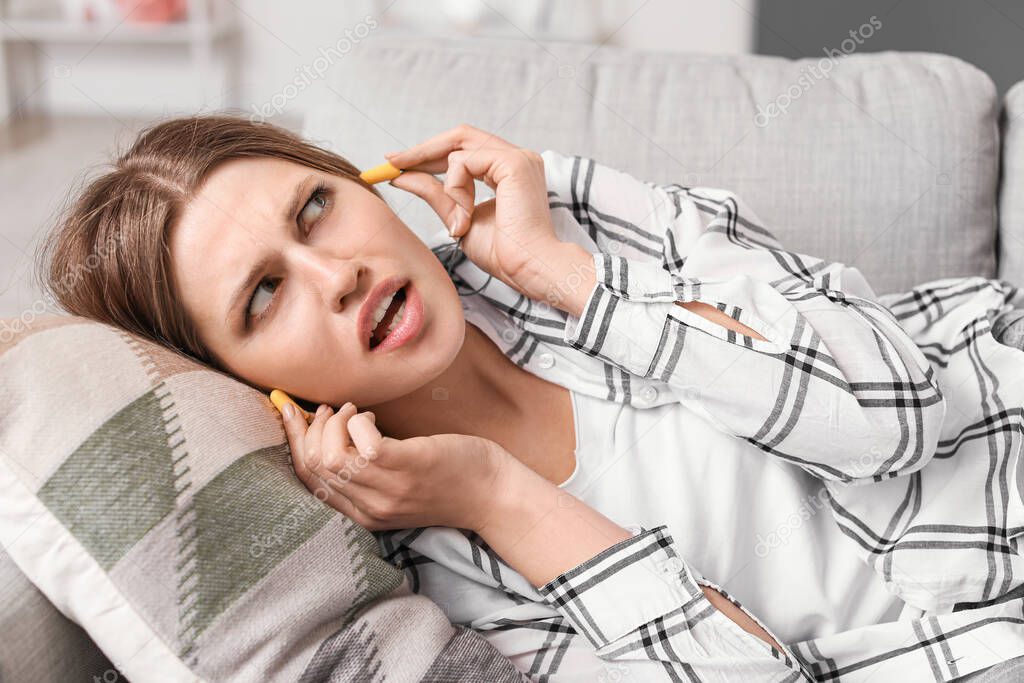 Young woman with ear plugs suffering from loud noise at home