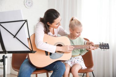 Özel müzik öğretmeni evde küçük bir kıza gitar dersi veriyor.