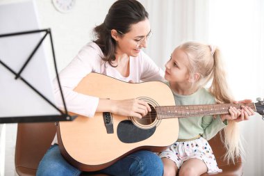 Özel müzik öğretmeni evde küçük bir kıza gitar dersi veriyor.