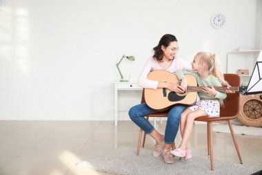 Özel müzik öğretmeni evde küçük bir kıza gitar dersi veriyor.