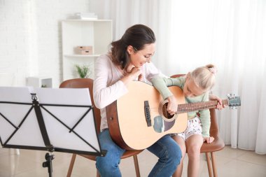 Özel müzik öğretmeni evde küçük bir kıza gitar dersi veriyor.