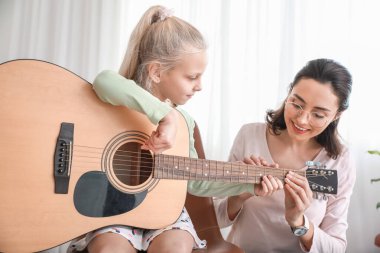 Özel müzik öğretmeni evde küçük bir kıza gitar dersi veriyor.