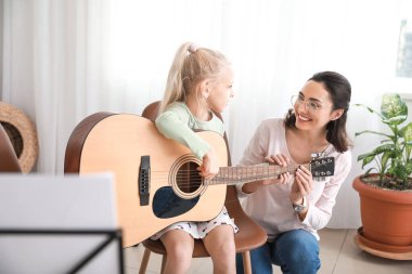 Özel müzik öğretmeni evde küçük bir kıza gitar dersi veriyor.