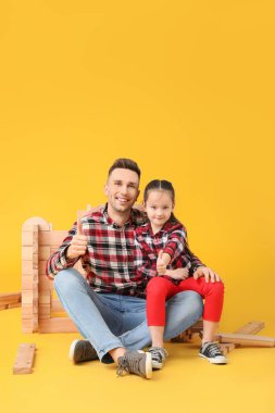 Baba ve küçük kızı, arka planda paravan evlerle oynuyorlar.