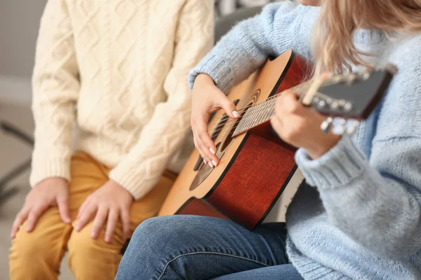 Private music teacher giving guitar lessons to little boy at home, closeup