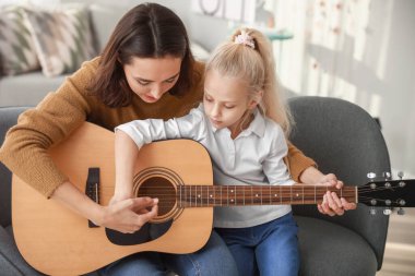 Özel müzik öğretmeni evde küçük bir kıza gitar dersi veriyor.