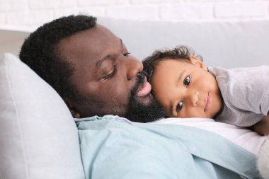 Kanepeye uzanmış, tatlı bebeği olan Afro-Amerikalı bir adam.