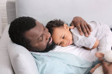 Kanepeye uzanmış, tatlı bebeği olan Afro-Amerikalı bir adam.