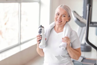 Spor salonunda bir şişe suyu olan olgun bir kadın.