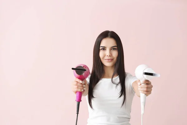 Beautiful young woman with hair dryers on color background