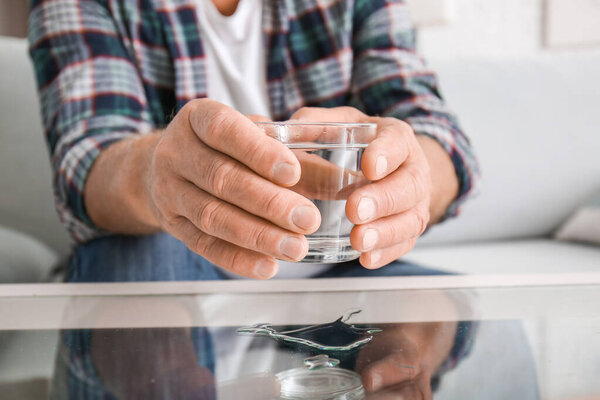 Senior man with Parkinson syndrome taking glass of water from table, closeup
