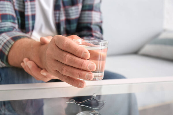 Senior man with Parkinson syndrome taking glass of water from table, closeup