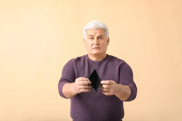 Sad senior man with empty purse on color background