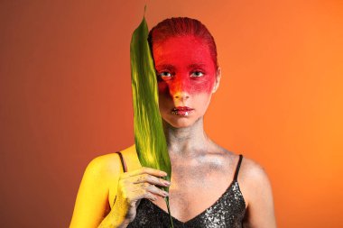 Sıra dışı makyajlı ve arka planda tropik yaprağı olan güzel bir kadın.