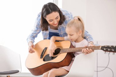 Özel müzik öğretmeni evde küçük bir kıza gitar dersi veriyor.