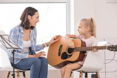 Özel müzik öğretmeni evde küçük bir kıza gitar dersi veriyor.