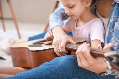 Özel müzik öğretmeni evde küçük bir kıza gitar dersi veriyor.
