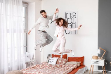 Mutlu genç çift evde yatakta zıplıyor.