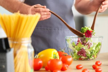 Yakışıklı aşçı mutfakta salata yapıyor, yakın plan.