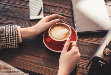 Ahşap masada lezzetli kapuçino içen bir kadın.