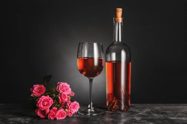 Masanın üzerinde bir şişe şarap, cam ve gül var.