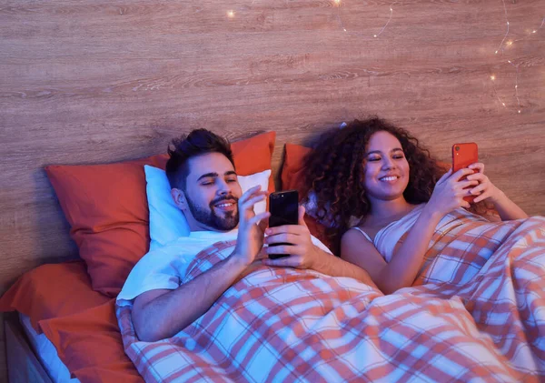 Happy young couple with mobile phones in bedroom