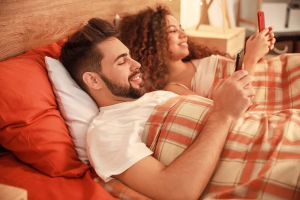 Happy young couple with mobile phones in bedroom