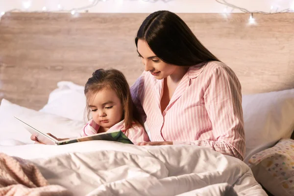 母と彼女の小さな娘は自宅で就寝時の物語を読んで — ストック写真