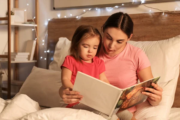 母と彼女の小さな娘は自宅で就寝時の物語を読んで — ストック写真