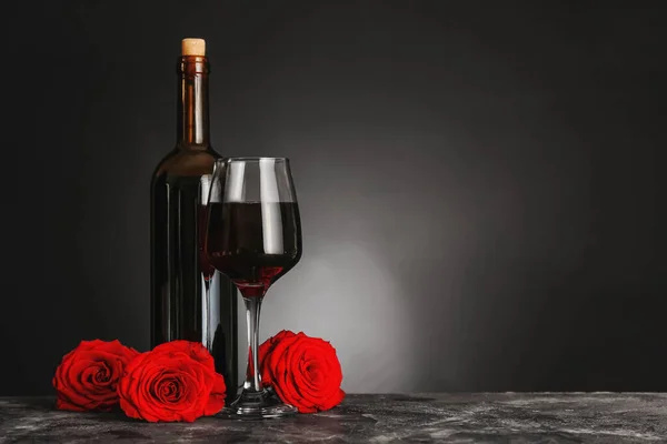 Bottle of wine, glass and roses on table against dark background