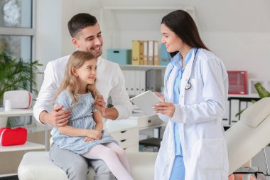 Küçük kızıyla birlikte çocuk doktorunu klinikte ziyaret eden bir adam.