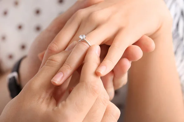 Young man putting ring on finger of his fiancee after marriage proposal, closeup