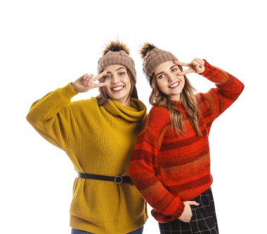 Beyaz arka planda zafer jesti gösteren kalın kazaklı genç kadınlar.