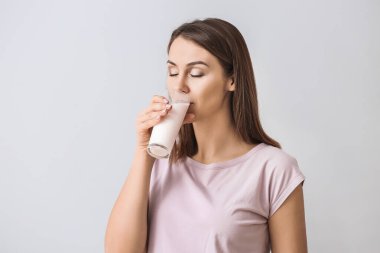 Açık arkaplanda bir bardak sütü olan güzel genç bir kadın.