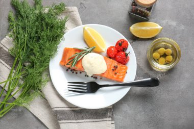 Gri arkaplanda pişmiş somon filetosu ve sos tabağı.