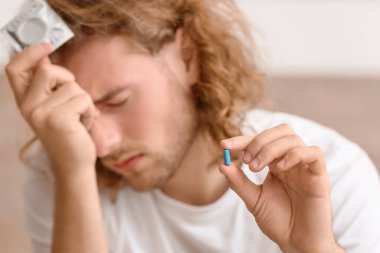 Oral ereksiyon bozukluğu ilacı ve prezervatifi olan üzgün bir adam yatak odasında.